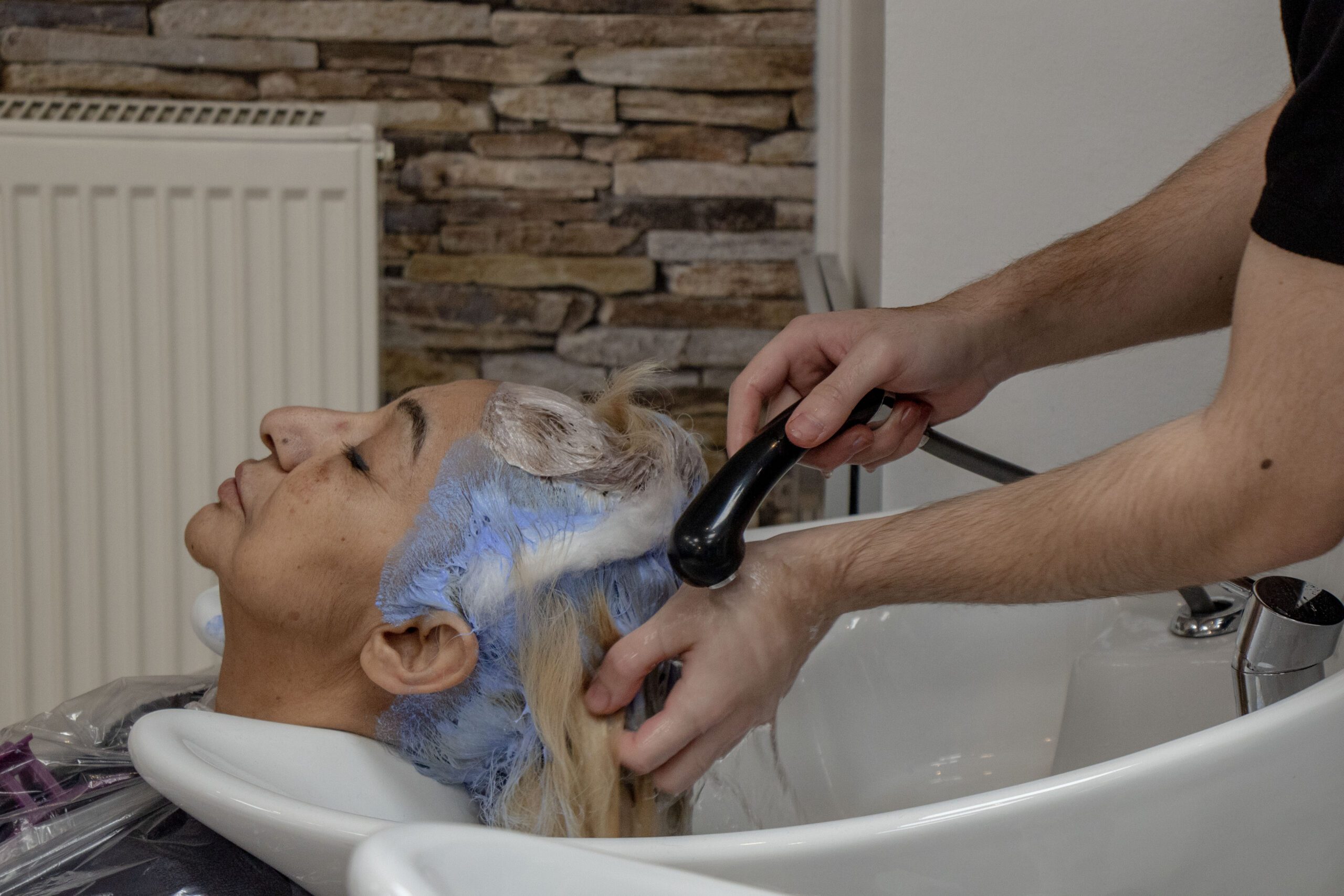 Friseurlehrling Aykut wäscht einer Kundin das Haarfarbemittel aus den Haaren
