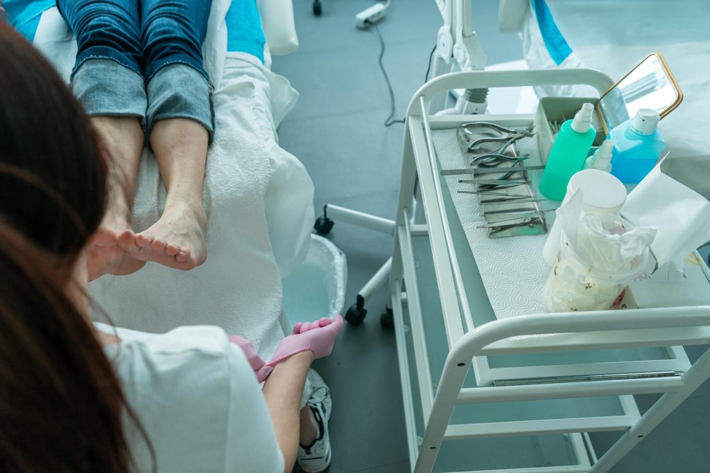 Hautzangen, Feilen und weitere Instrumente für die Pediküre liegen auf einem kleinen Tisch neben der Behandlungsliege.