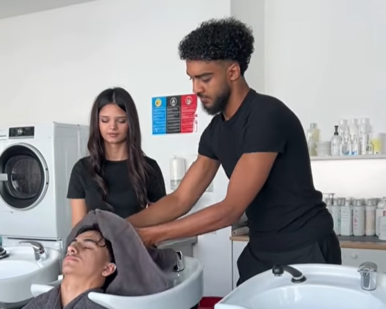 Lehrlinge der überbetrieblichen Lehrausbildung zum:zur Friseur:in beim Haarewaschen eines weiteren Lehrlings
